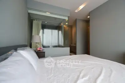 Modern bedroom with glass partition and ensuite bathroom, featuring sleek design and neutral tones.