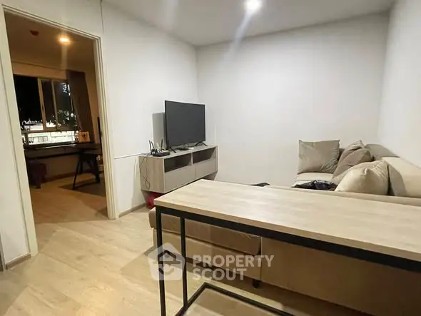 Modern living room with cozy sectional sofa and flat-screen TV, open doorway to adjacent room.