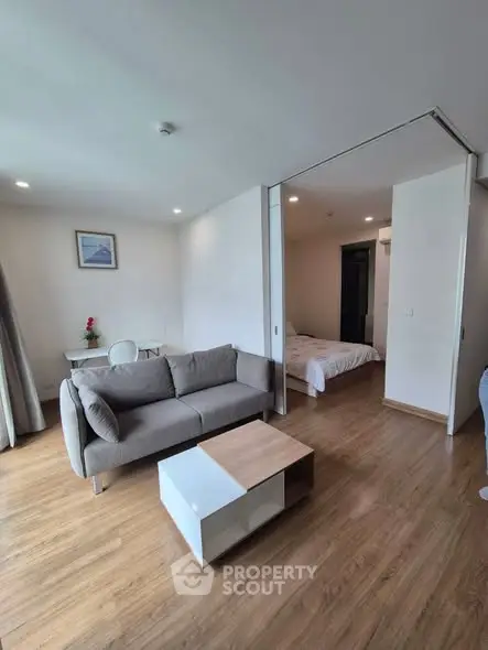 Modern living room with cozy sofa and open view to bedroom, featuring elegant wooden flooring.