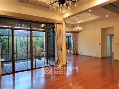 Spacious living room with elegant chandeliers and large windows opening to a garden view.