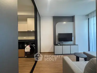 Modern living room with sleek furniture and open kitchen layout, featuring a washing machine and TV setup.