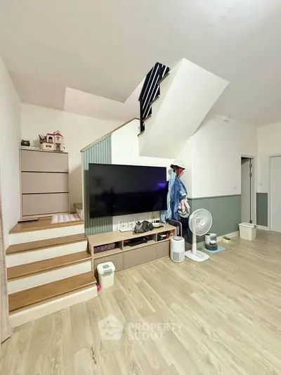 Modern living room with stylish staircase and wooden flooring, featuring a large TV and contemporary decor.