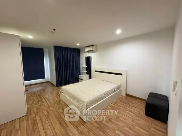 Spacious modern bedroom with wooden flooring and elegant blue curtains.