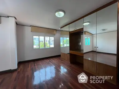 Spacious living room with polished hardwood floors, ample natural light, and large mirrored wall creating an expansive feel in a modern home.