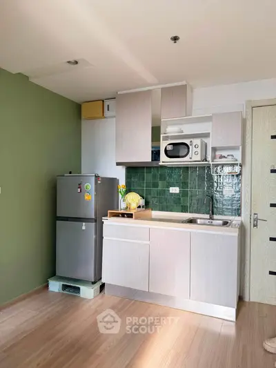 Modern kitchen with green backsplash, compact fridge, and microwave in cozy apartment.