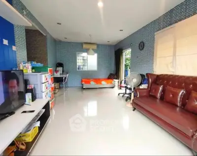 Spacious living room with modern decor and natural light, featuring a leather sofa and entertainment area.