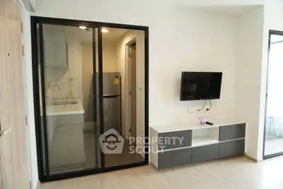 Modern apartment living room with sleek TV setup and compact kitchen area.