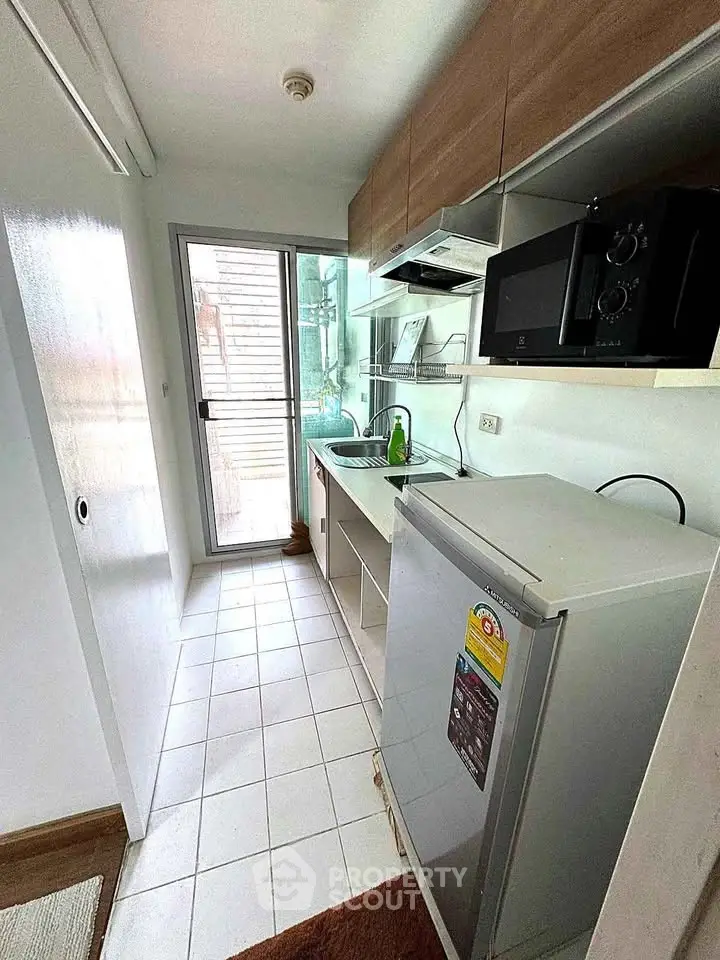 Compact kitchen with modern appliances and natural light, featuring a microwave and mini fridge.