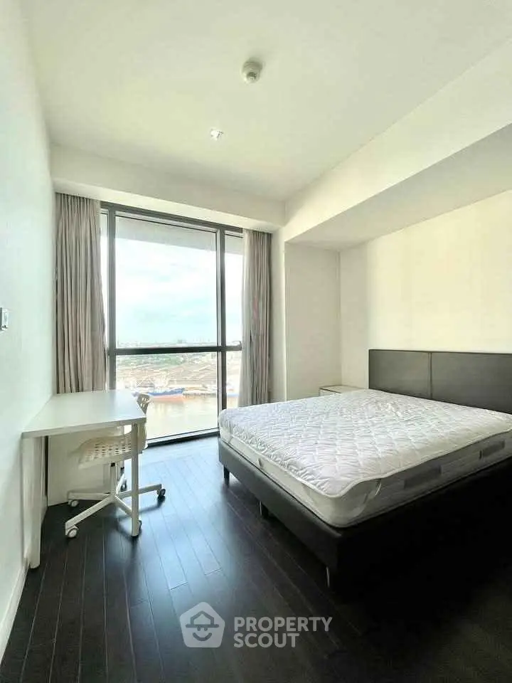 Bright bedroom with large window and modern furnishings in a high-rise apartment.