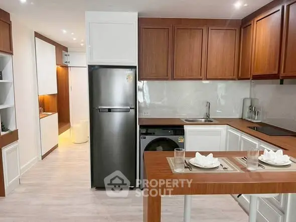 Modern kitchen with wooden cabinets, stainless steel fridge, and compact washing machine.