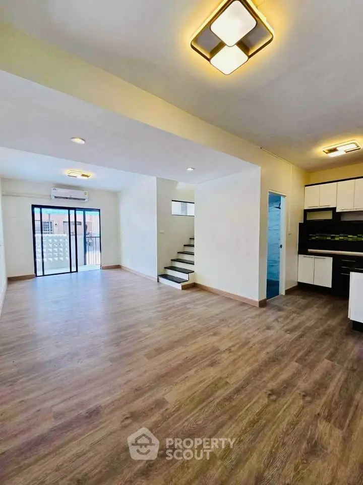Spacious open-plan living area with modern kitchen and stylish lighting, featuring wooden flooring and balcony access.