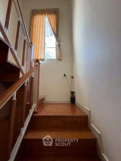 Charming wooden staircase with natural light from window, perfect for cozy home ambiance.