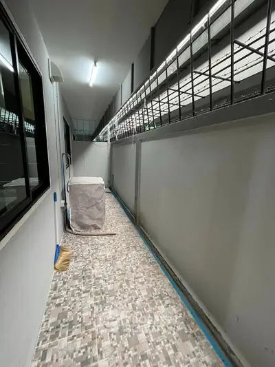 Narrow tiled corridor with covered appliance and barred window, ideal for utility space.