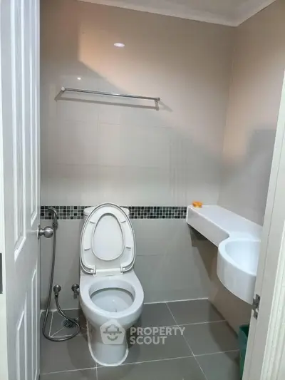 Modern bathroom with sleek design featuring a toilet, wall-mounted sink, and towel rack.