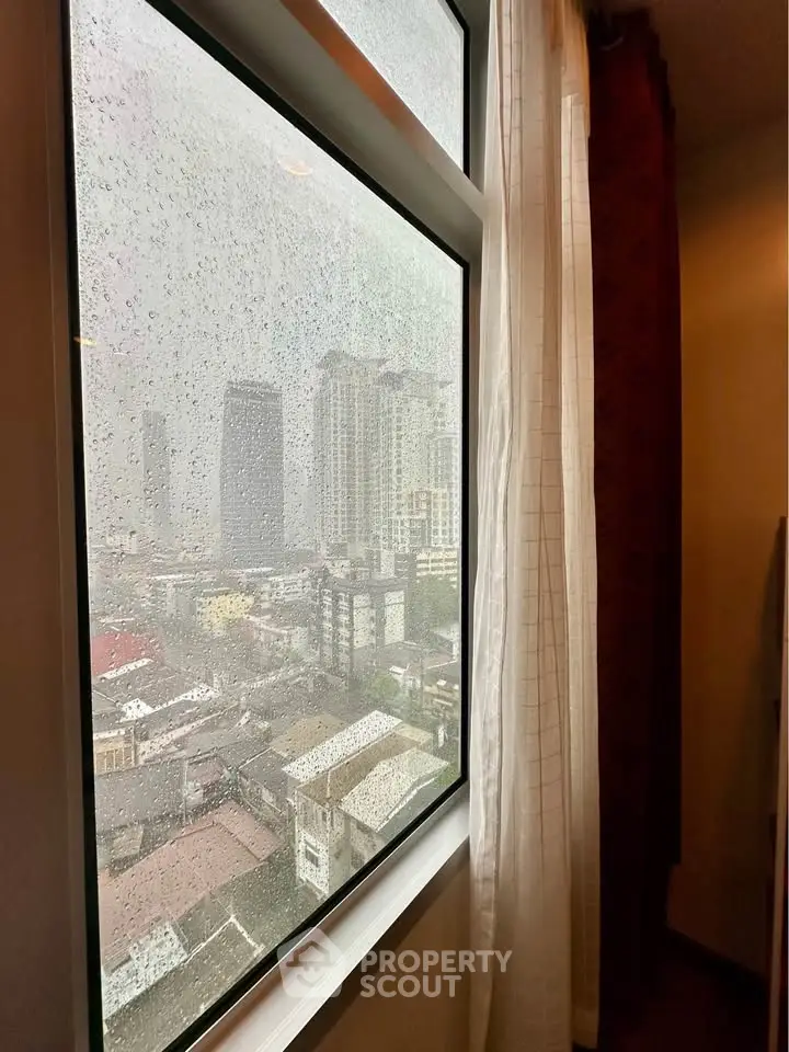 Stunning cityscape view from a high-rise apartment window on a rainy day, showcasing urban living.