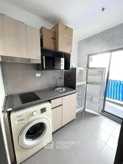 Modern kitchen with washing machine and open fridge, featuring sleek cabinetry and tiled flooring.