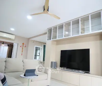 Modern living room with beige sofa, large TV, and glass cabinet