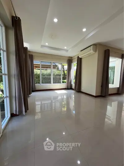 Spacious living room with large windows and garden view, featuring modern air conditioning and elegant curtains.
