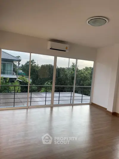 Spacious living room with large windows offering a serene view of greenery, perfect for relaxation.