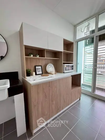Modern kitchen with sleek cabinetry and microwave, featuring open shelving and stylish decor.