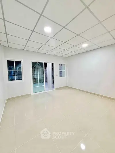 Spacious empty room with tiled floor and sliding glass doors in modern apartment.