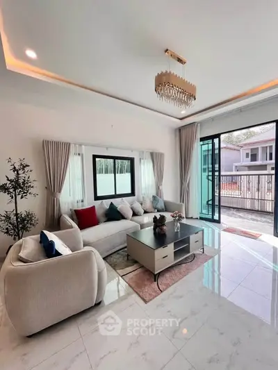 Luxurious living room with elegant chandelier and spacious seating area, opening to a sunny balcony view.