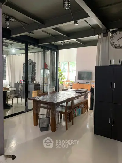 Modern open-plan living space with dining area and glass partition, featuring sleek furniture and natural light.
