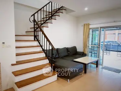 Modern living room with staircase and cozy sofa, featuring natural light from large windows.