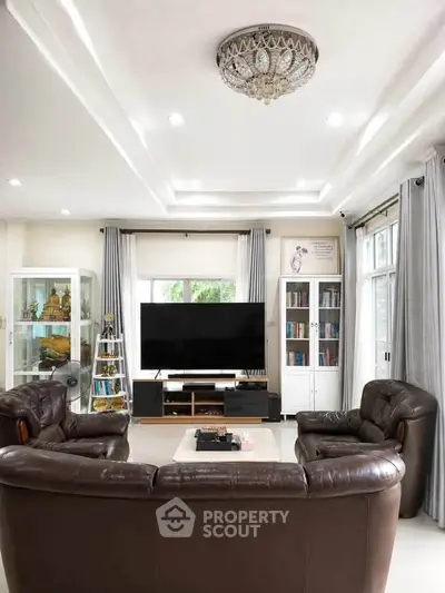 Luxurious living room with leather sofas, large TV, and elegant chandelier