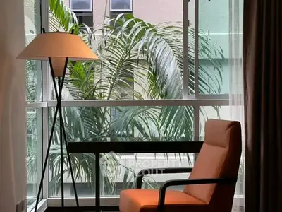 Stylish interior with modern chair and floor lamp by large window with lush greenery view.