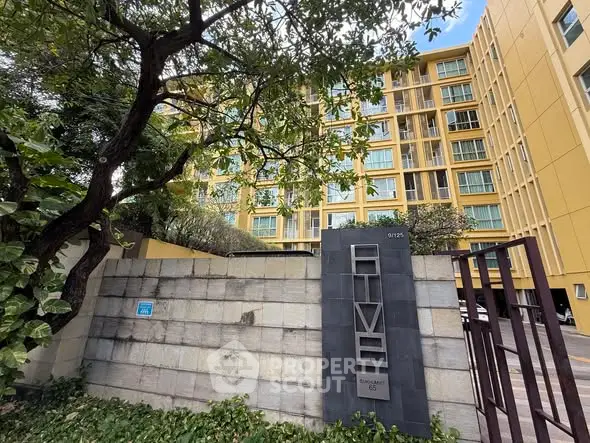 Modern yellow apartment building with lush greenery and secure entrance.
