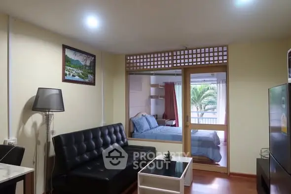Modern living room with black leather sofa and view into cozy bedroom