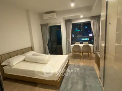 Modern bedroom with city view, featuring a cozy bed and dining area, perfect for urban living.