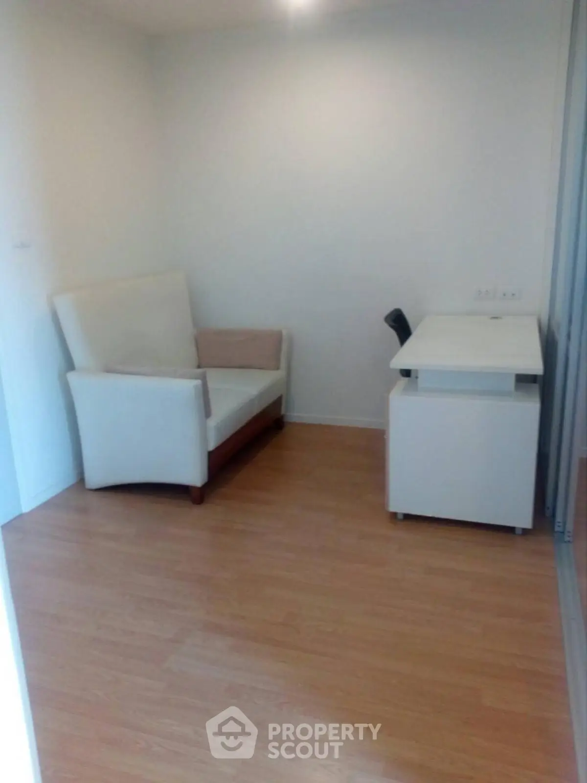 Cozy small study room with a white armchair and desk on wooden flooring.