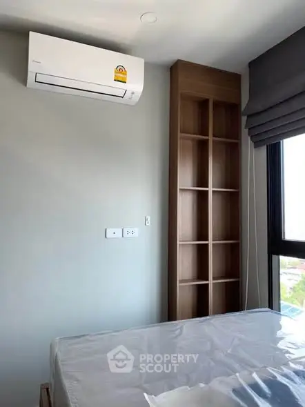 Modern bedroom with air conditioning and built-in shelving, featuring a large window for natural light.