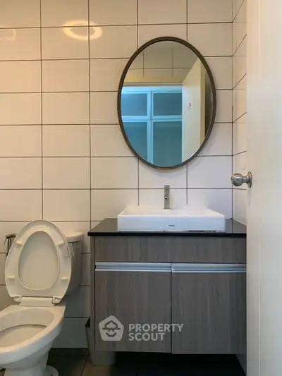Modern bathroom with sleek vanity and round mirror, featuring contemporary design and neutral tones.