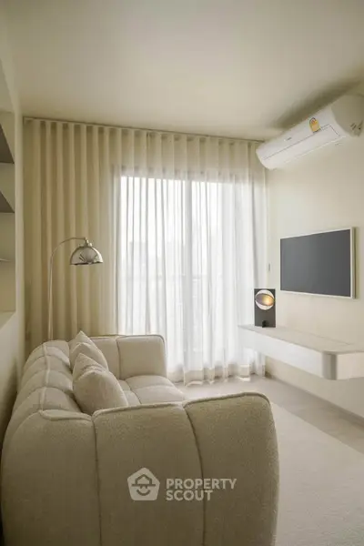 Modern living room with cozy sofa, wall-mounted TV, and large window with sheer curtains.