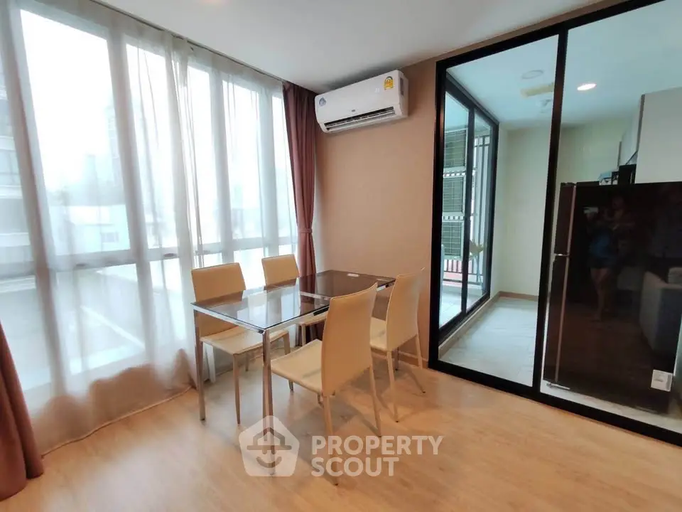 Modern dining area with glass table and beige chairs, featuring large windows and air conditioning.