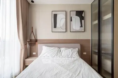 Modern bedroom with stylish decor and natural light, featuring abstract art and cozy bedding.