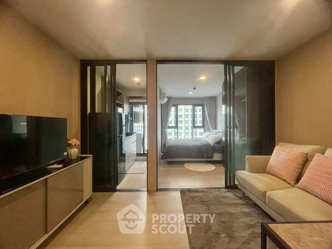 Modern living room with glass partition leading to cozy bedroom in urban apartment.
