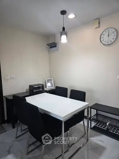 Modern dining area with sleek table and black chairs, featuring a wall clock and minimalist decor.