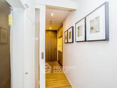Modern hallway with wooden flooring and framed art, leading to a cozy interior space.