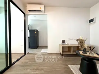 Modern living room with sleek wooden flooring and minimalist decor, featuring a view into a compact kitchen area.