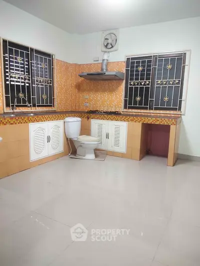 Unique kitchen with integrated toilet, tiled walls, and ventilation fan.