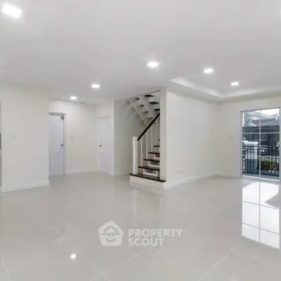 Spacious modern living room with sleek tile flooring and staircase, abundant natural light, and outdoor access.
