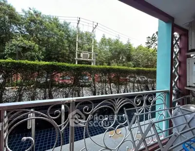 Charming balcony with ornate railing overlooking lush greenery and street view.