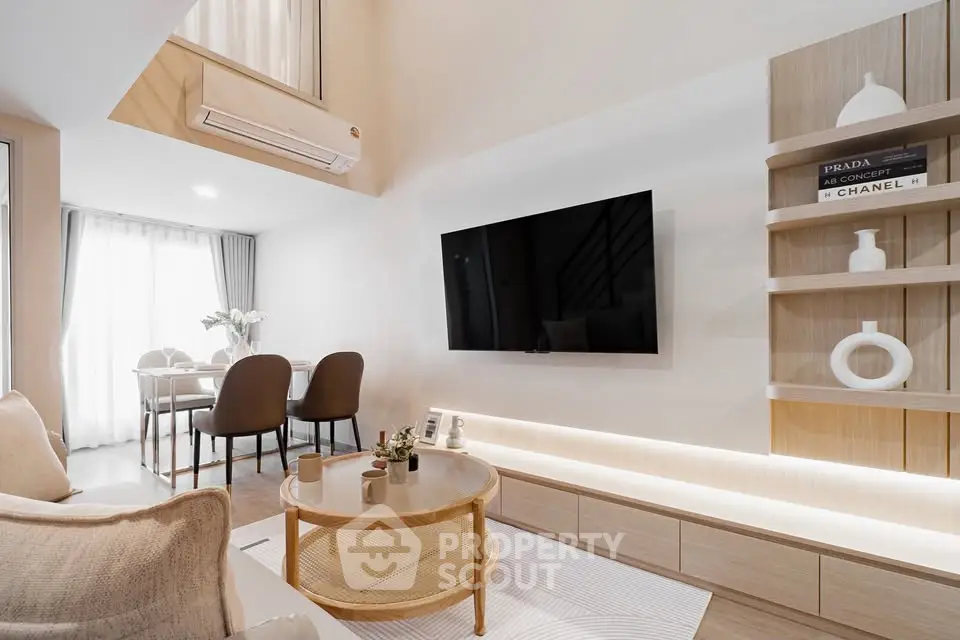 Modern living room with stylish decor, open layout, and dining area, featuring a wall-mounted TV and elegant shelving.