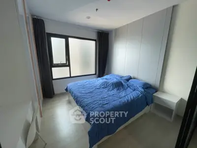 Modern bedroom with blue bedding and large window, perfect for relaxation.