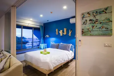 Modern bedroom with blue accent wall and large window offering scenic views.