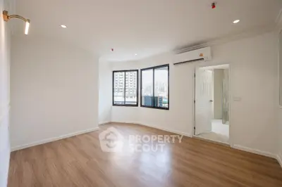 Spacious empty room with wooden flooring and large windows in a modern apartment.